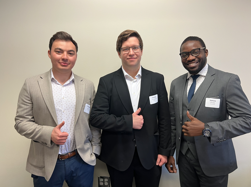Three students stand against a white wall. They are each smiling and holding a thumbs-up. 