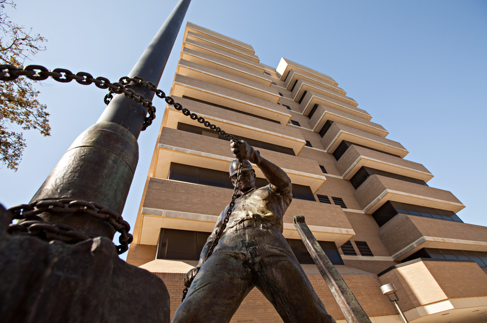 A picture of a bronze statue is taken looking up at the statue and the building that stands behind it. 