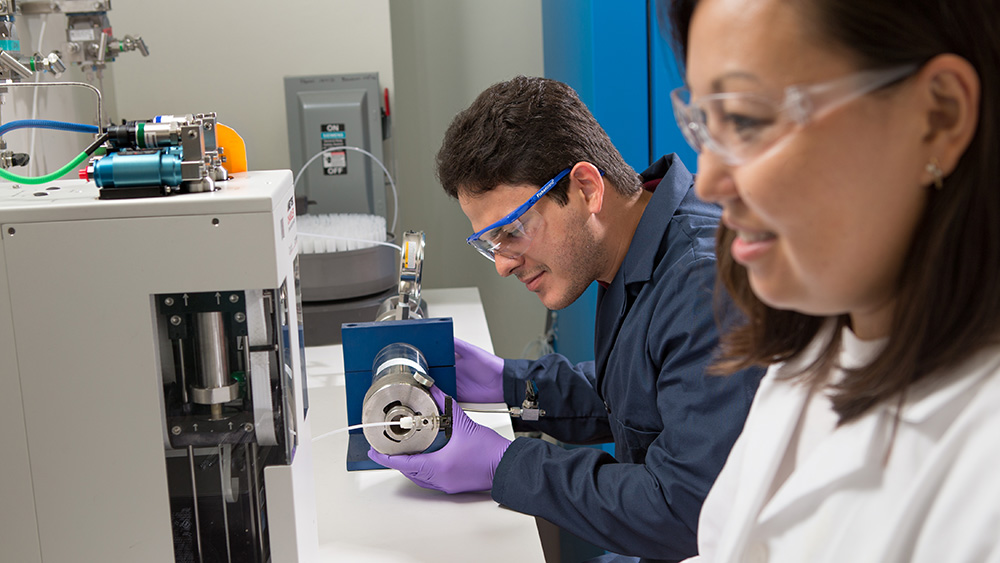 two graduate students, one male and one female, dressed in safety attire working with equipment in a Texas A&amp;M petroleum engineering lab