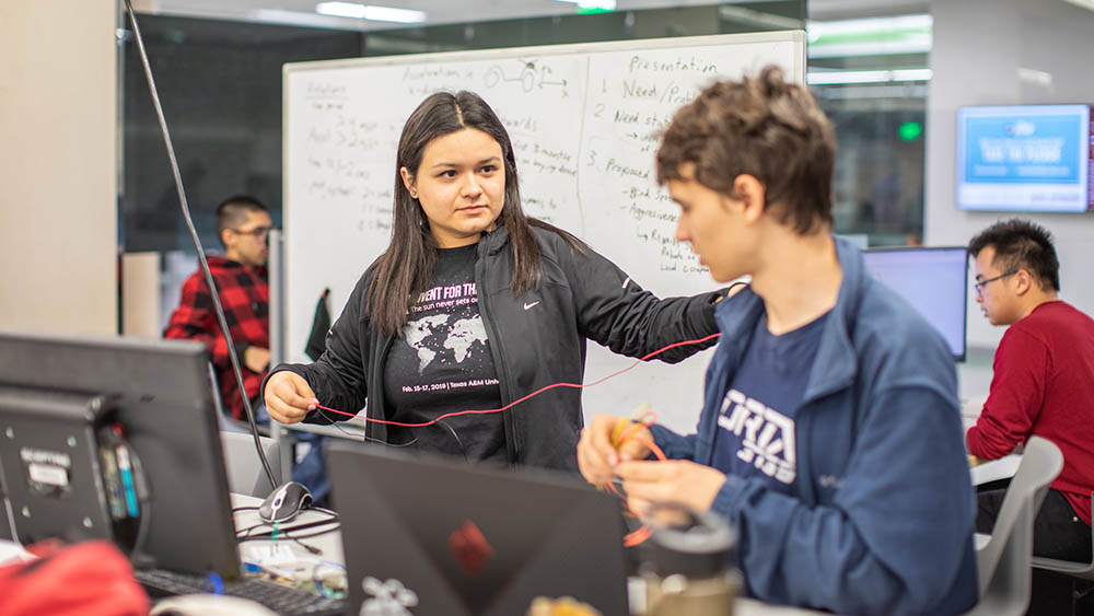 Female student in Invent for the Planet t-shirt works with electrical wiring on a design project with male student.