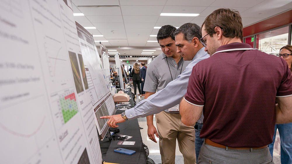 A showcase judge pointing at a poster while students look on.