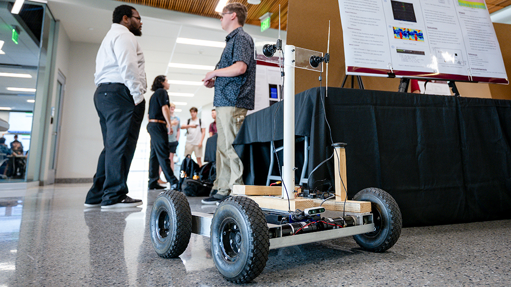 Robot with wheels on the floor with students in the background.
